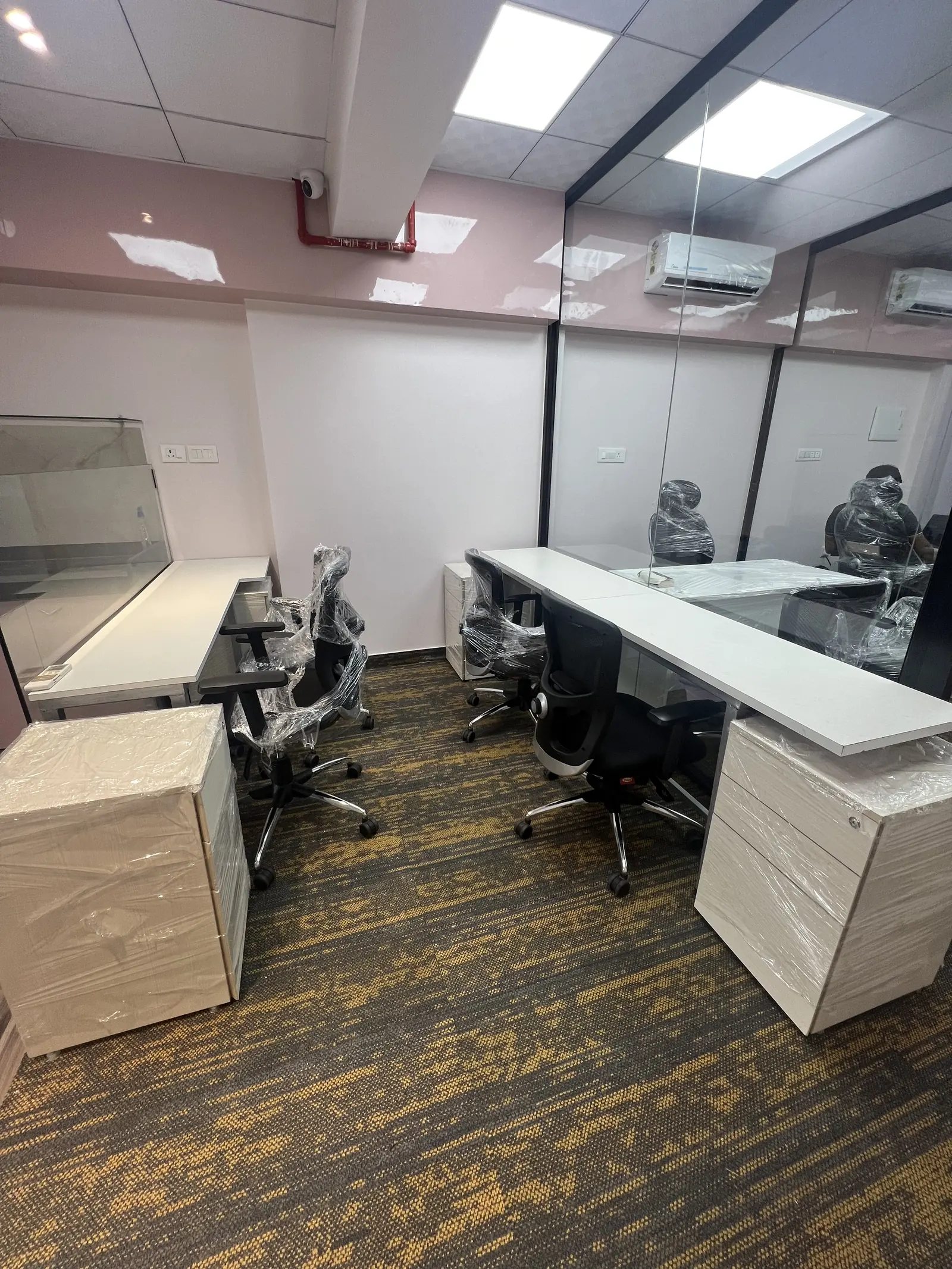 Glass-walled cabin with a long white desk, mesh chairs and a split AC