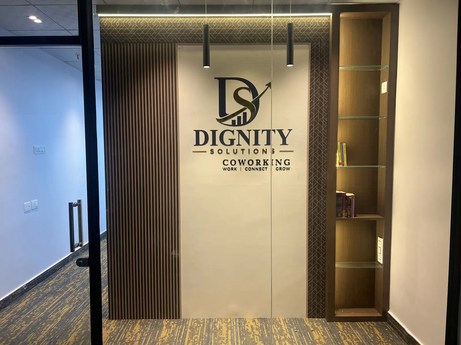 Glass entrance to Unit 142 with the backlit Dignity Solutions Coworking sign on a slatted wall