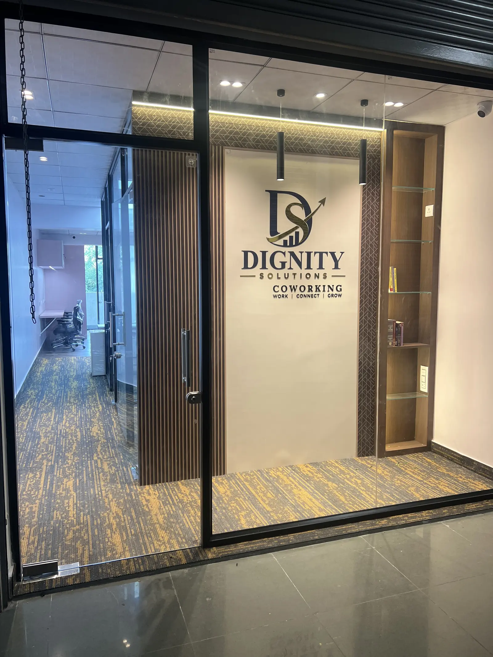 Open glass door into Dignity Solutions Coworking, with the logo wall and the corridor beyond