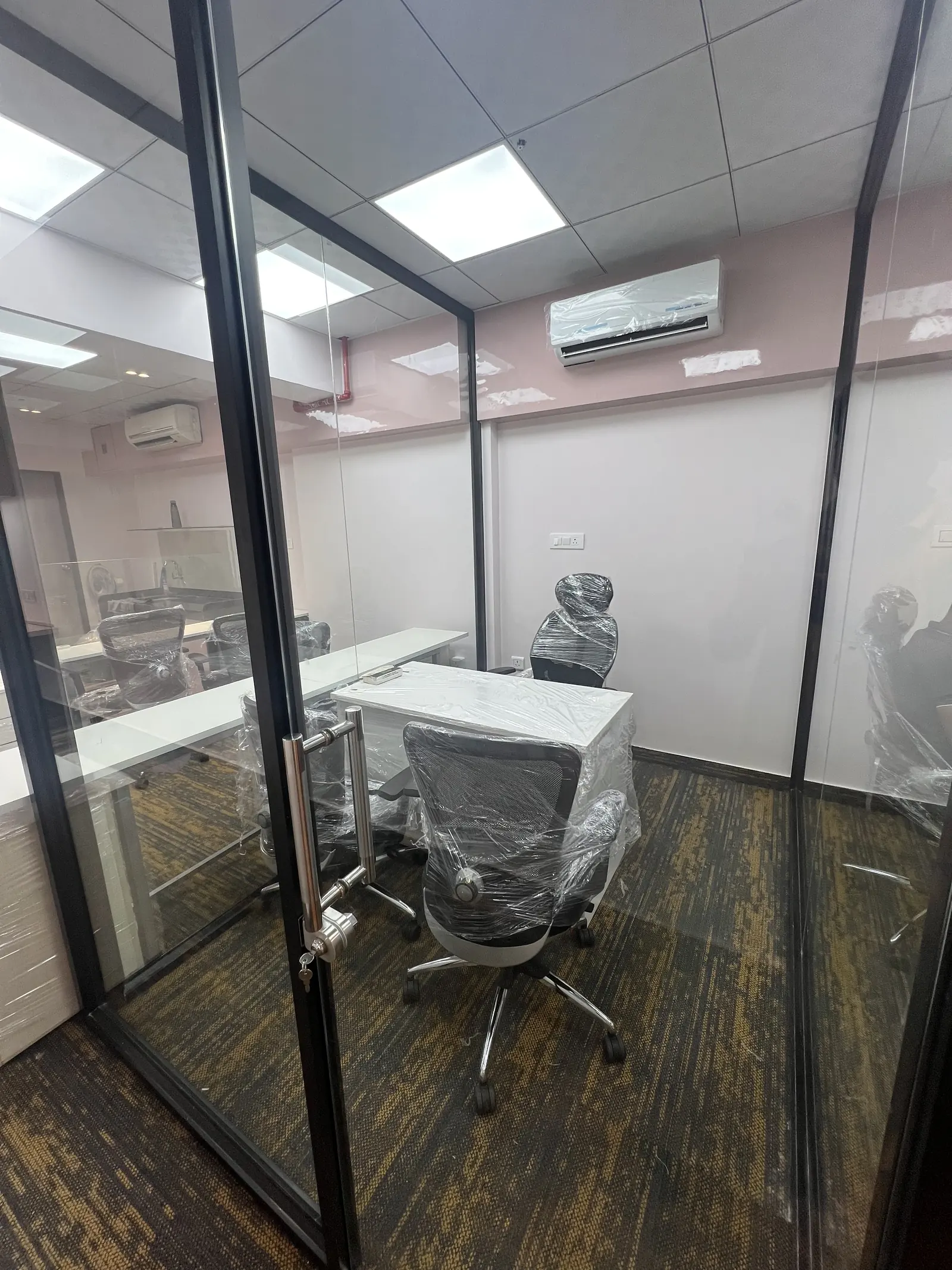 Glass manager cabin with a white desk and a high-back mesh chair